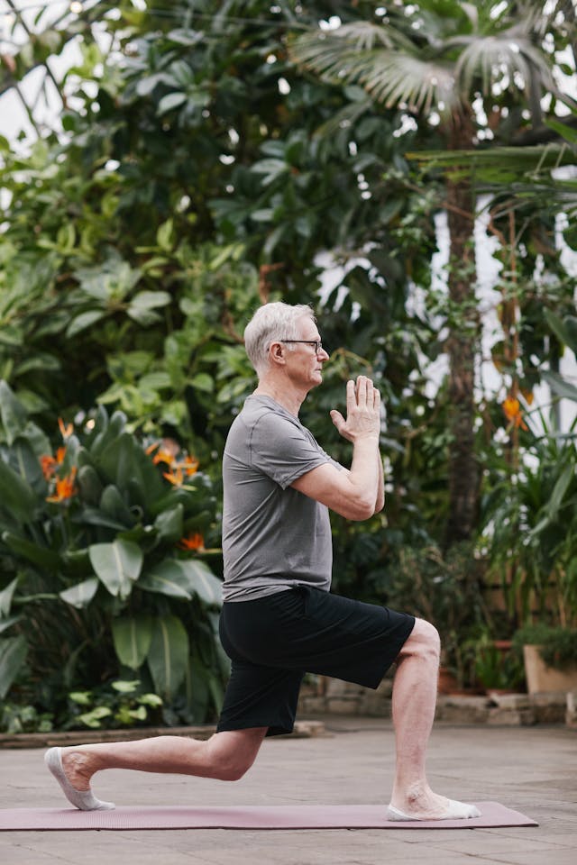 Homme senior de profil qui fait une fente avant avec en fond des plantes