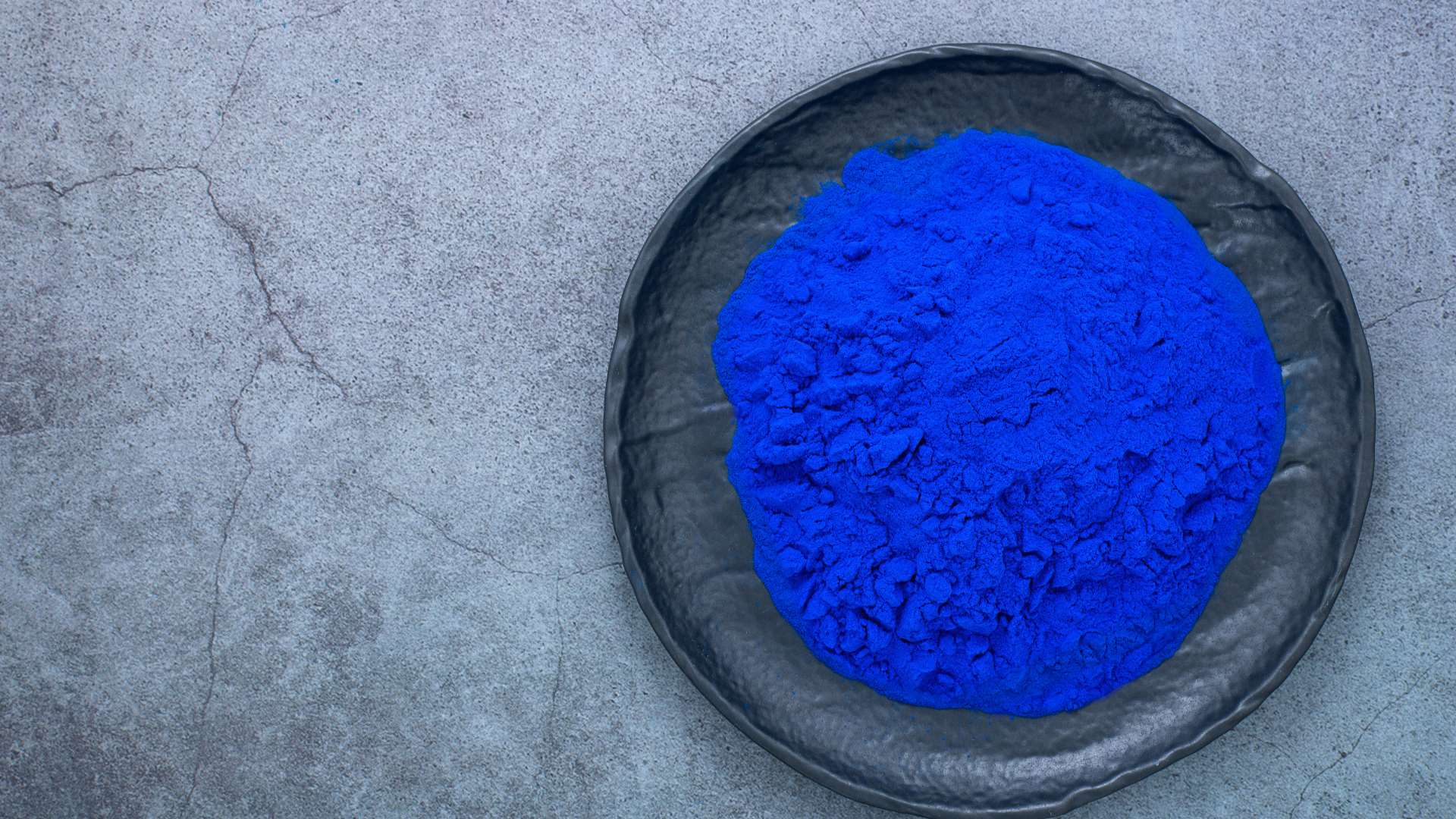 Phycocyanine bleu roi dans assiette grise anthracite sur marbre gris plus clair