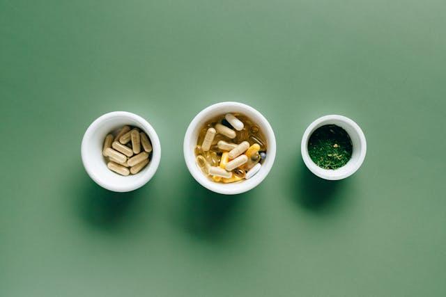 Trois ramequins blancs vu de haut avec des gélules et capsules sur fond vert